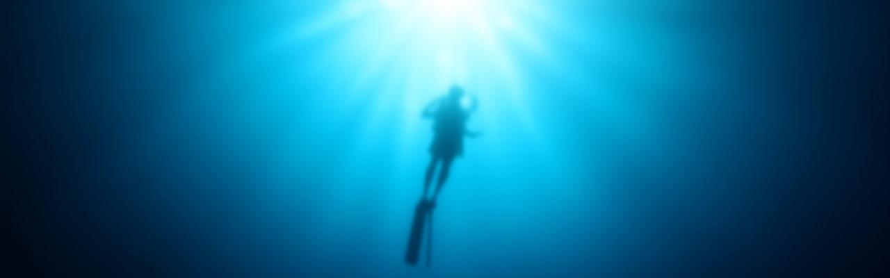 Silueta de buzo nadando elegantemente en aguas claras con rayos de sol penetrando desde la superficie.